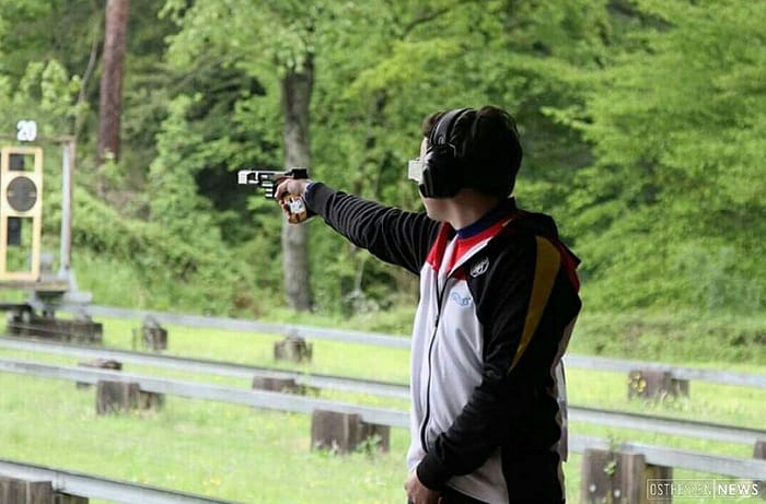 Sportschütze mit Gehörschutz zielt mit der Sportpistole auf die Klappscheibe